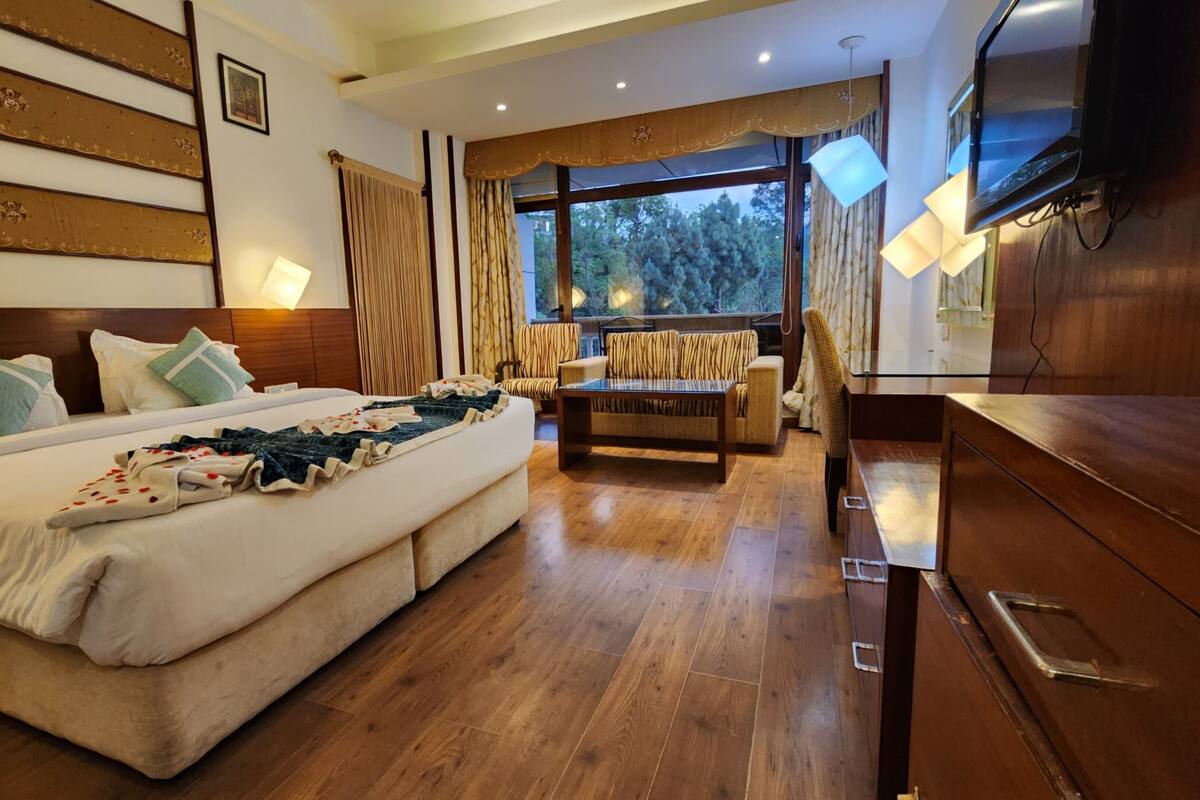 Habitación de hotel con una cama grande, un aparador de madera, un sofá y un televisor fijado a la pared.