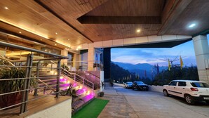 Un edificio moderno con una escalera que conduce a un balcón, un estacionamiento con coches y una vista de montañas al fondo.