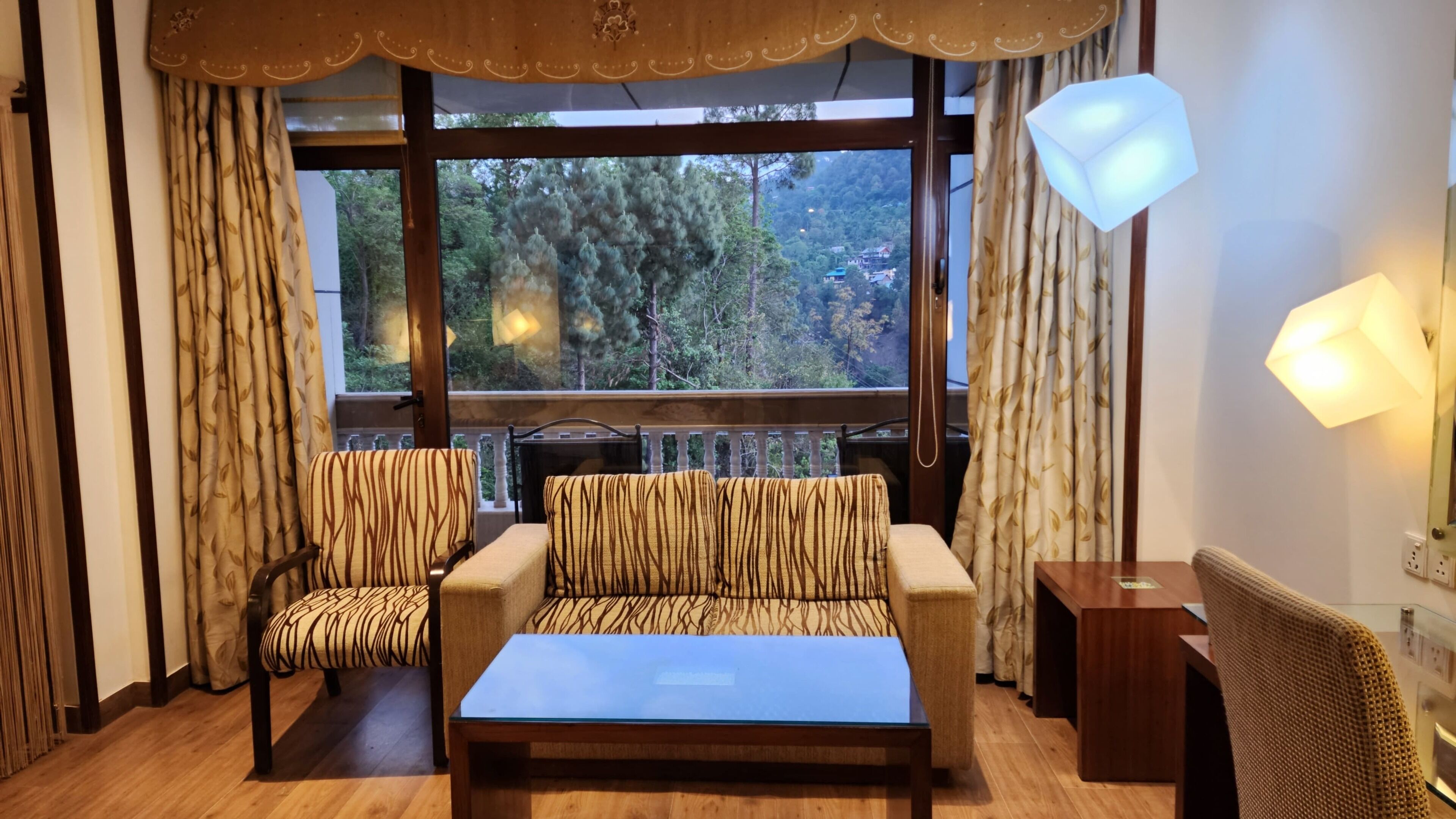 Una habitación con sofá, dos sillones, una mesita y vista a un bosque a través de amplias ventanas.