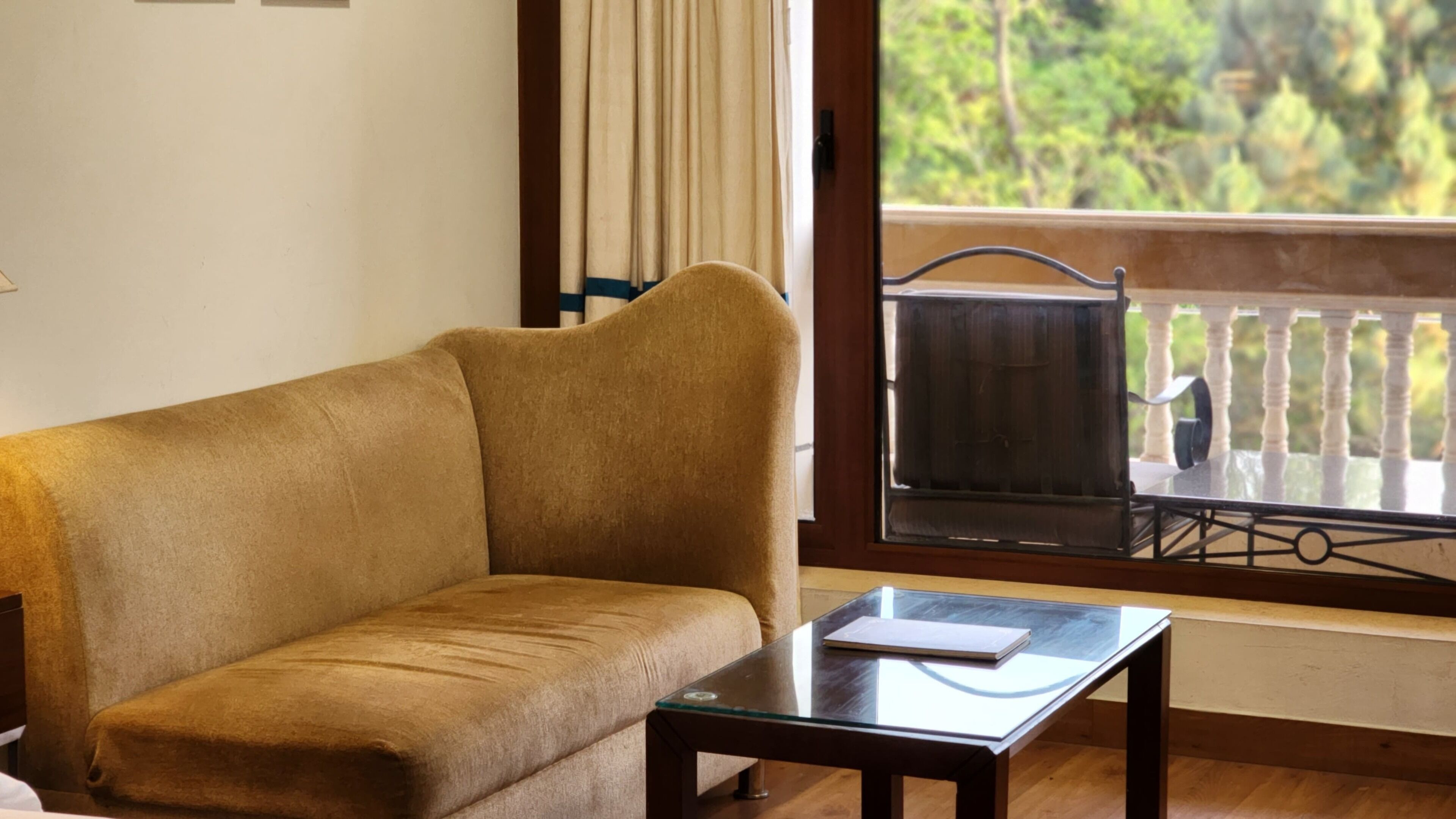 A living room with a sofa, a glass table, and a view of a balcony with a railing.