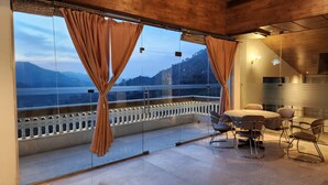 Un balcón con baranda de vidrio y cortinas, una mesa con sillas y vistas a montañas.