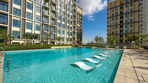 A swimming pool with clear blue water, surrounded by a modern apartment building with balconies.