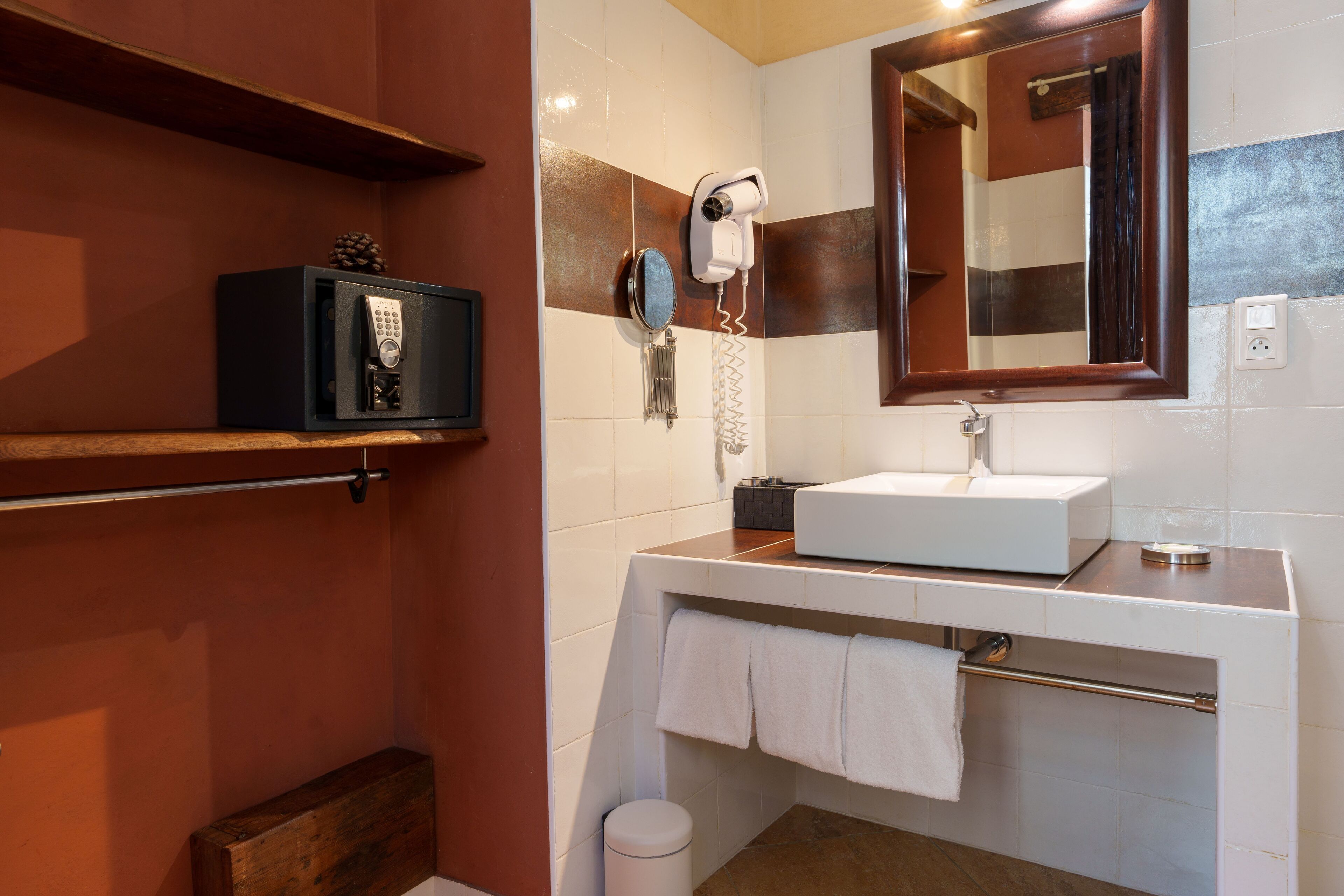 A modern bathroom with a built-in safe, a hairdryer, and a large mirror.