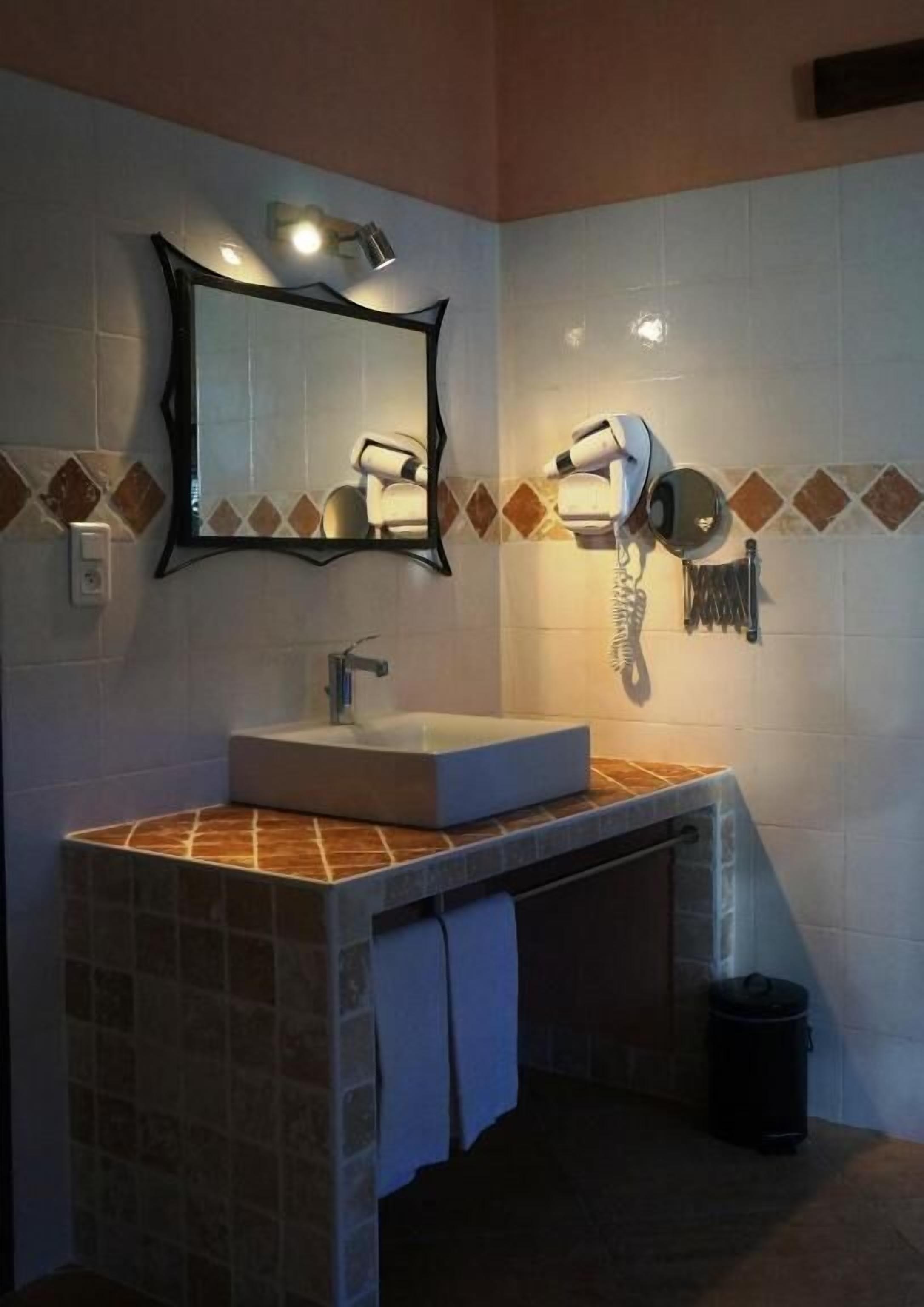Casa de banho com lavatório, espelho e secador de cabelo fixado na parede.