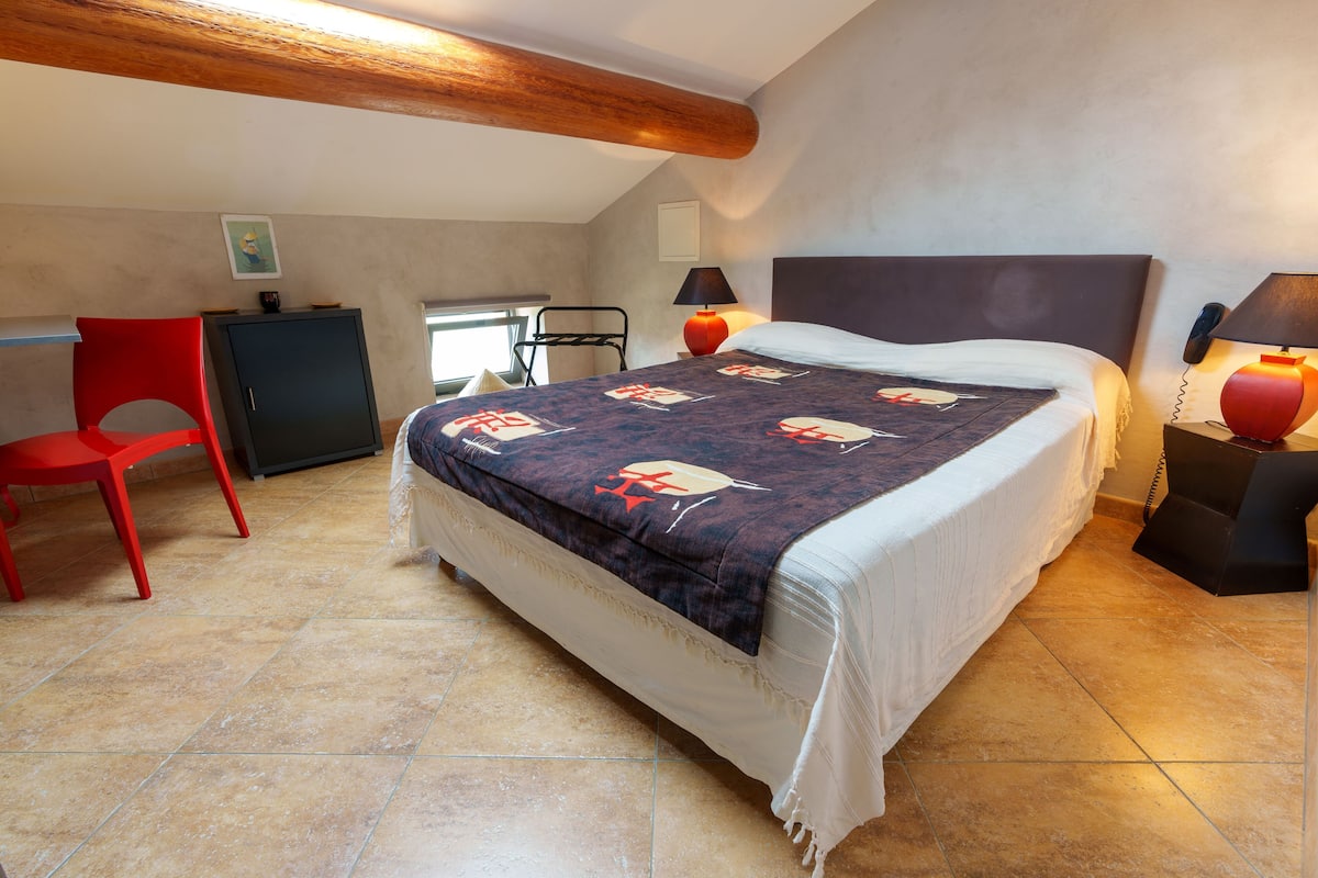 A bedroom with a bed, a red chair, a desk, and a lamp.
