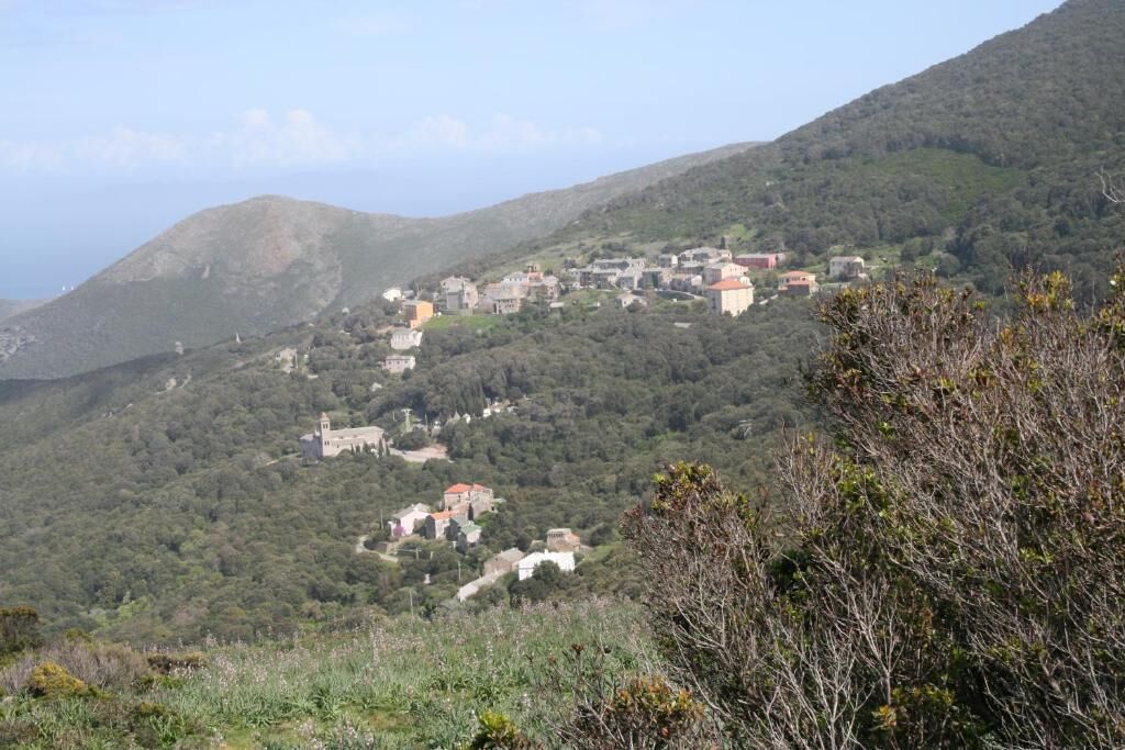 A hillside village with buildings scattered across the terrain, surrounded by greenery and hills.