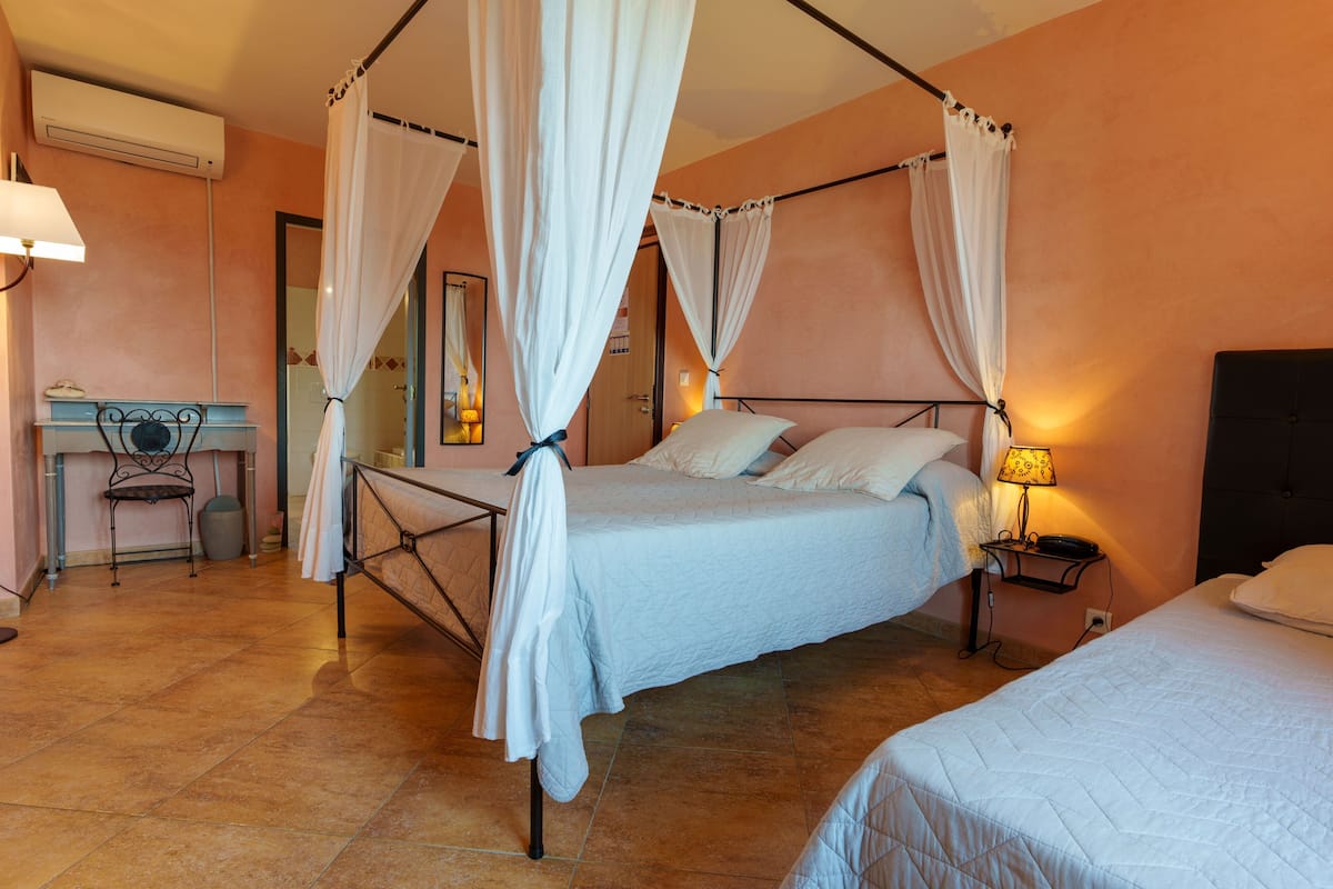 A bedroom with a four-poster bed, a desk with a chair, and a nightstand with a lamp.