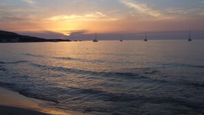 Un atardecer sobre un mar tranquilo con varios veleros anclados.