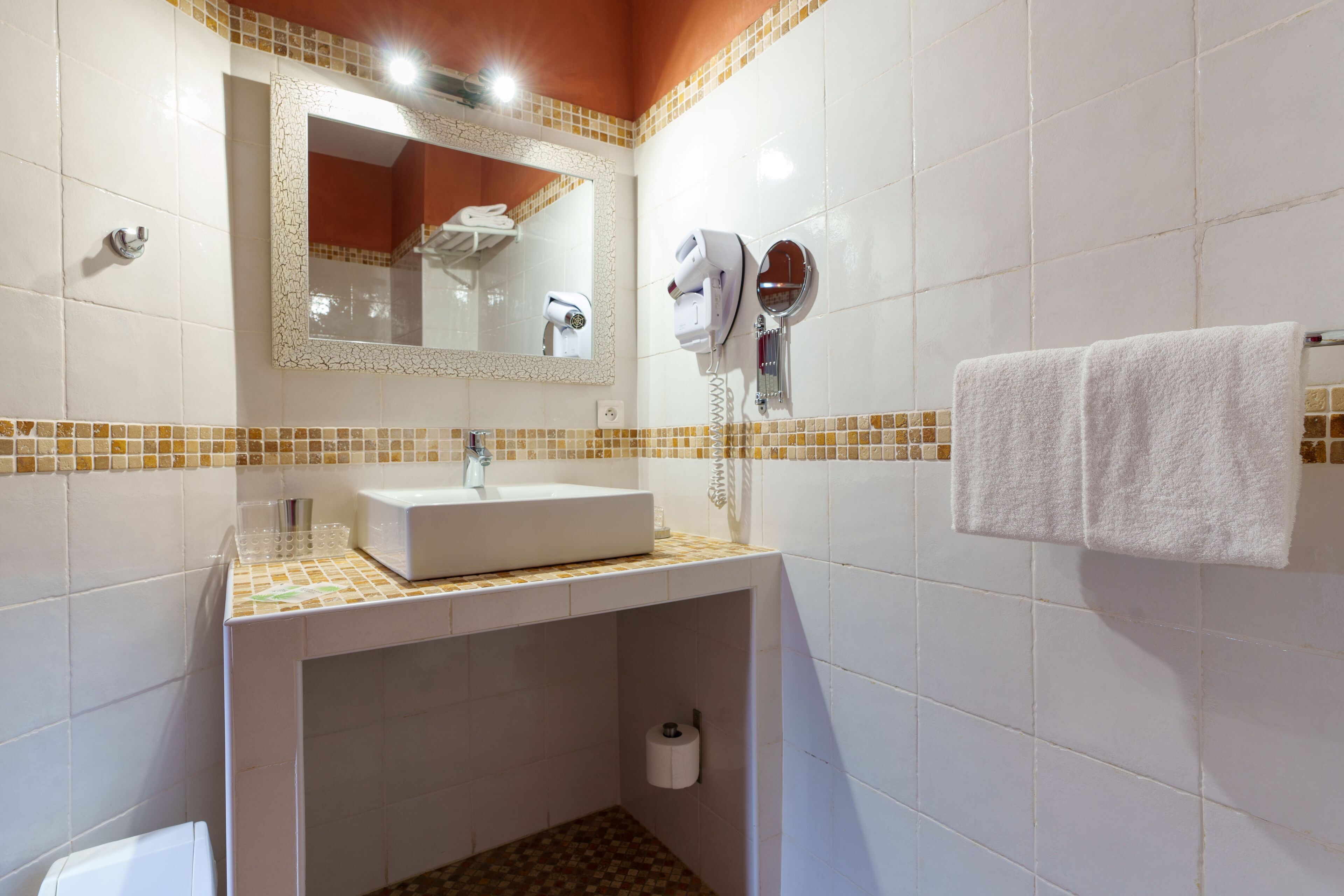 Uma casa de banho com uma pia branca, um espelho, um porta-toalhas e uma sanita.