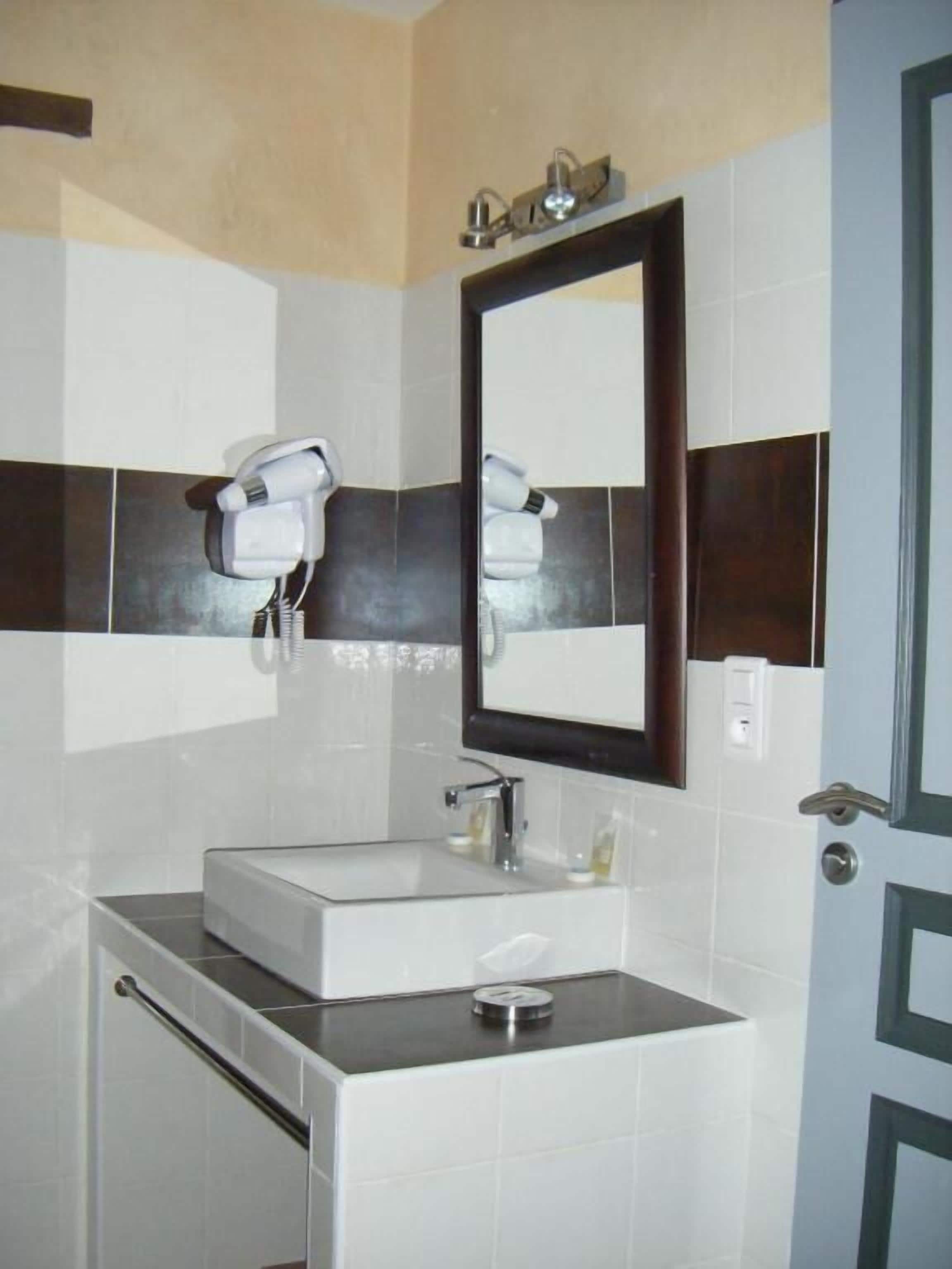Un baño con lavamanos blanco, un espejo y un perchero para toallas.