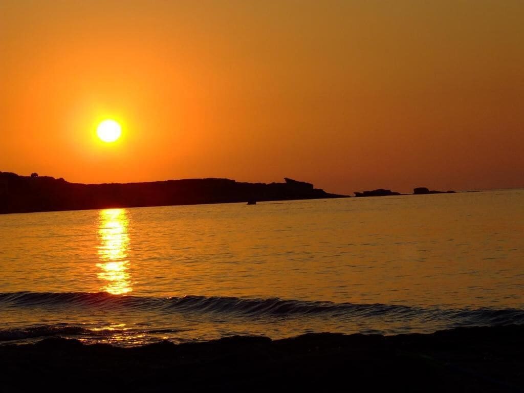 Um pôr do sol sobre um mar calmo, com o contorno de terra ao fundo.