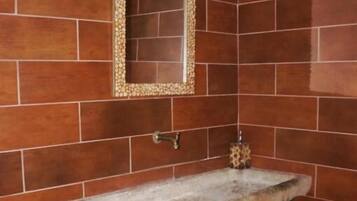 A bathroom with a stone sink, a mirror with a decorative frame, and brown tiled walls.