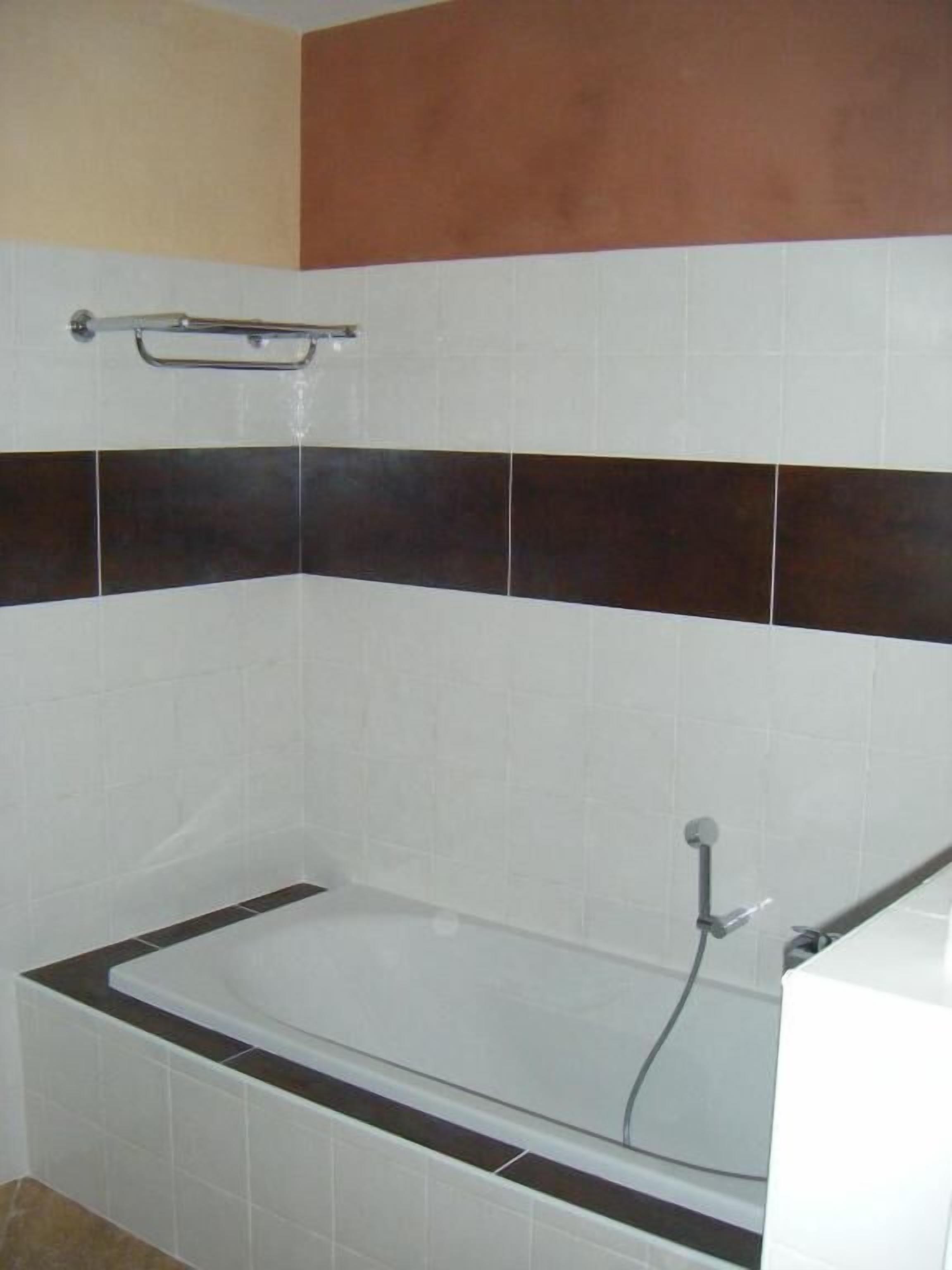 A bathroom with a bathtub, white and dark brown tiles, and a metal grab bar above the tub.