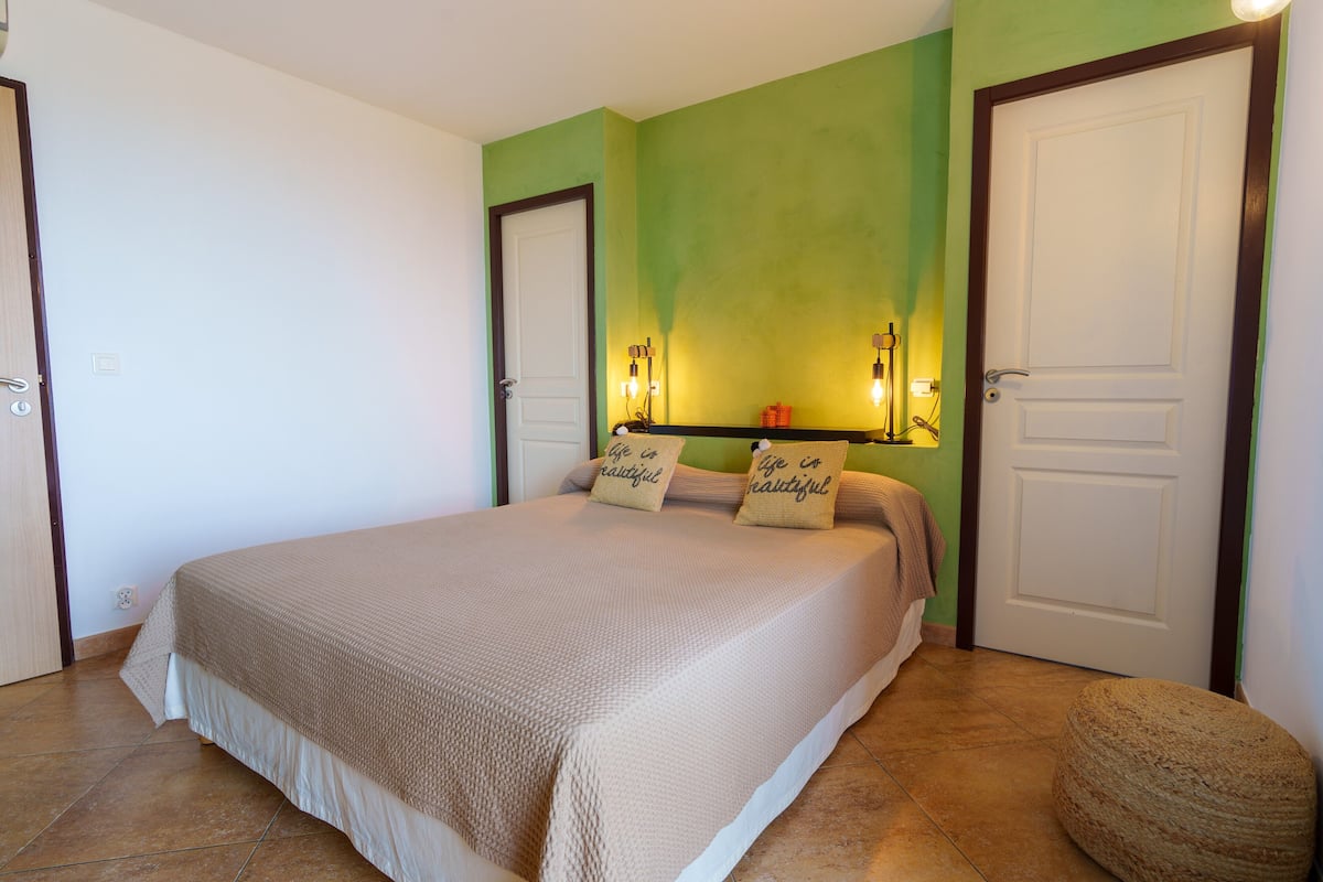 A bedroom with a bed, two doors, and a wall-mounted light fixture.