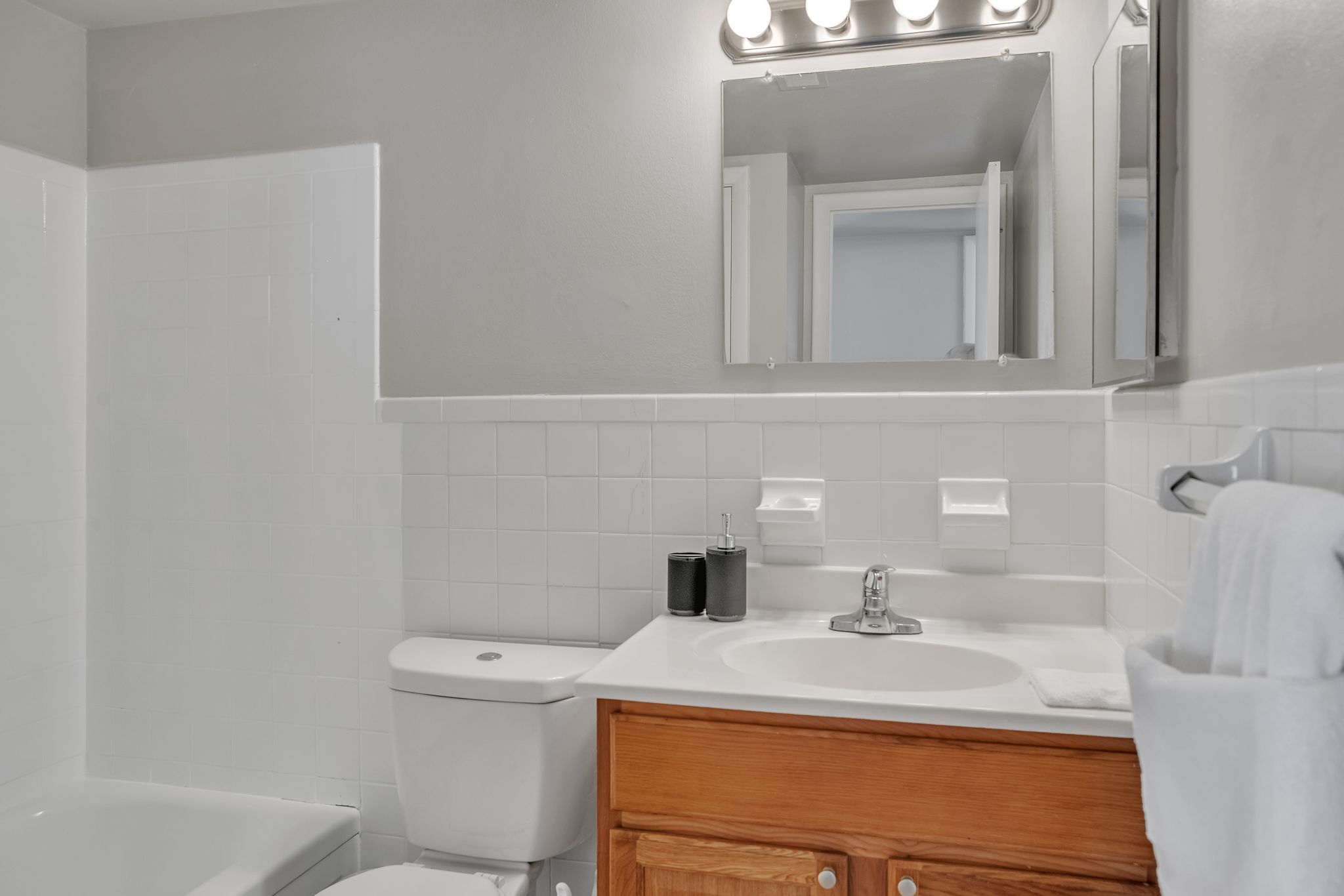 Une salle de bain moderne avec des toilettes blanches, un lavabo surmonté d’un miroir et un meuble-lavabo en bois.