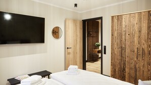 A modern hotel room with a large bed, a flat-screen TV mounted on the wall, a wooden wardrobe, and a small seating area with a magazine. - Binnendiek Resort Büsum Haus 4 - Apartment 2 (Büsum)