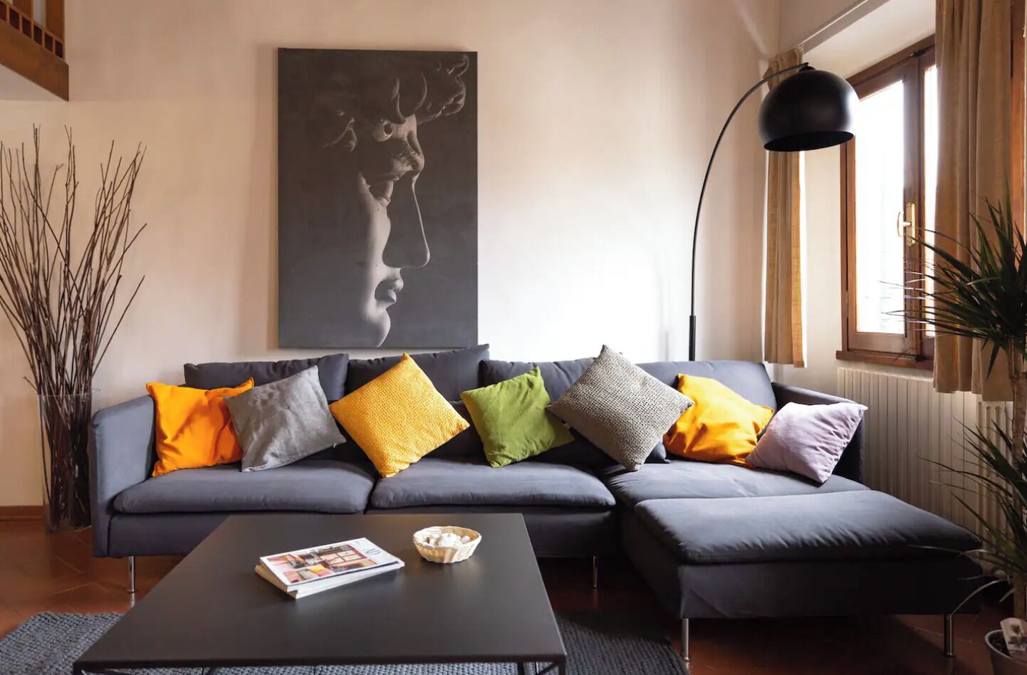 A modern living room with a grey sectional sofa, a coffee table with magazines, a large abstract painting, and a floor lamp.