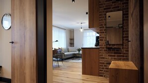 Una sala de estar moderna con piso de madera, un sofá, una mesa de centro y una zona de cocina con pared de ladrillo y armarios de madera.