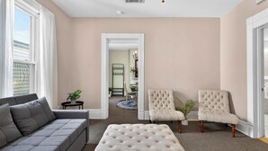 A living room with a grey sofa, a beige ottoman, and two armchairs.