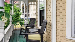 A porch with two chairs, a potted plant, and a window with blinds.