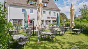 An outdoor seating area with tables and chairs, a building with a sign reading "Altes Buckhaus," and a well-maintained lawn. - Pension Altes Backhaus (Herzogenaurach)