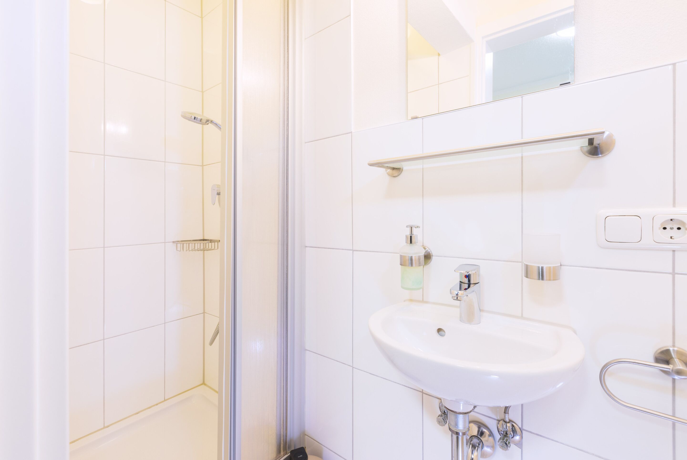 Un baño moderno con cabina de ducha de vidrio, un lavabo blanco y un espejo sobre el lavabo.