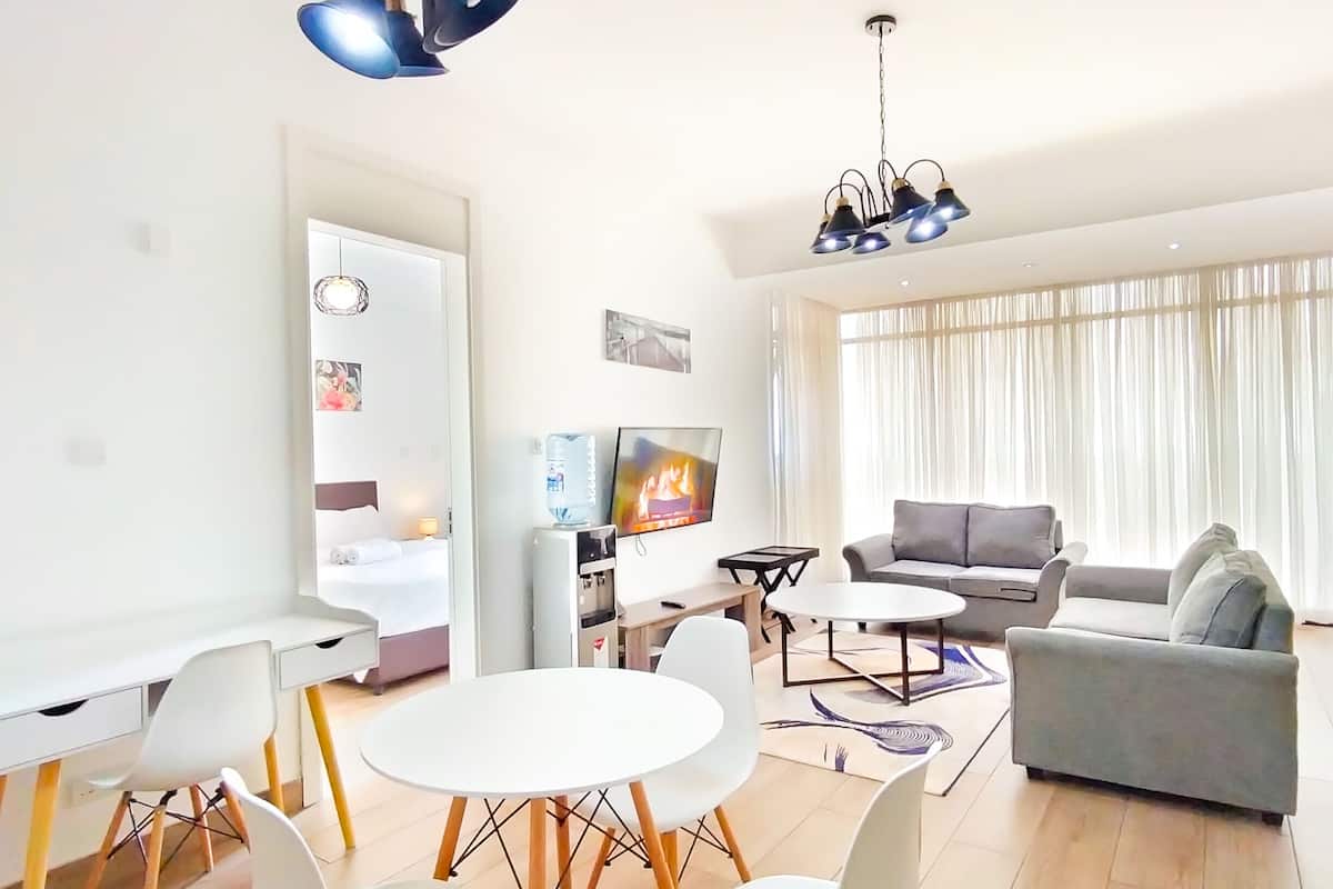 Ein modernes Wohnzimmer mit einem grauen Sofa, weißen Sesseln, einem runden Tisch und einem Fernseher.