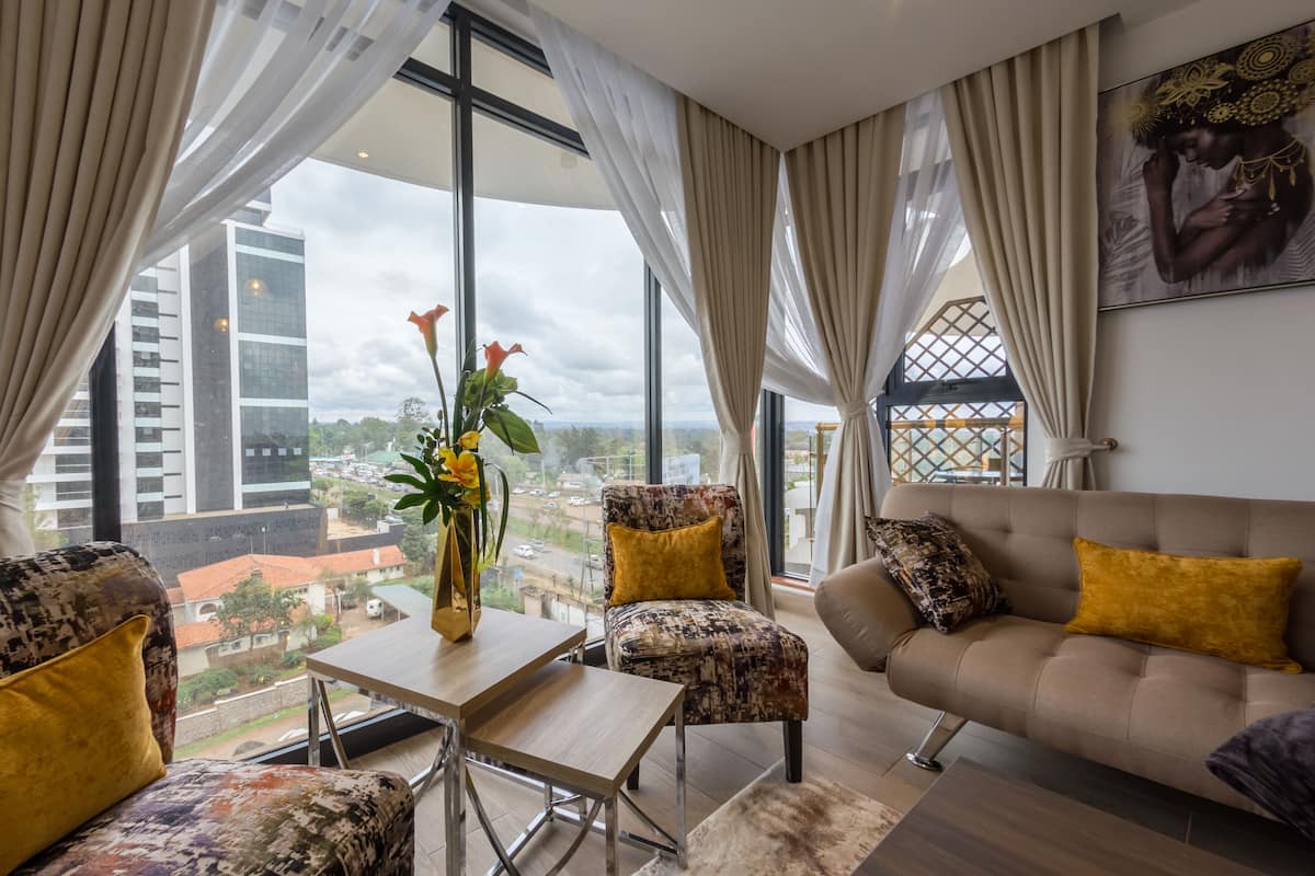 Ein modernes Wohnzimmer mit einer Couch, Sesseln und einem Couchtisch. Große Fenster bieten Blick auf die Stadt.