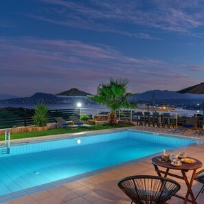 A swimming pool with lounge chairs and a table with cups and plates, overlooking a cityscape and mountains at dusk. - Villa Roula 3BR Seaview Villa in Chania (Chania)