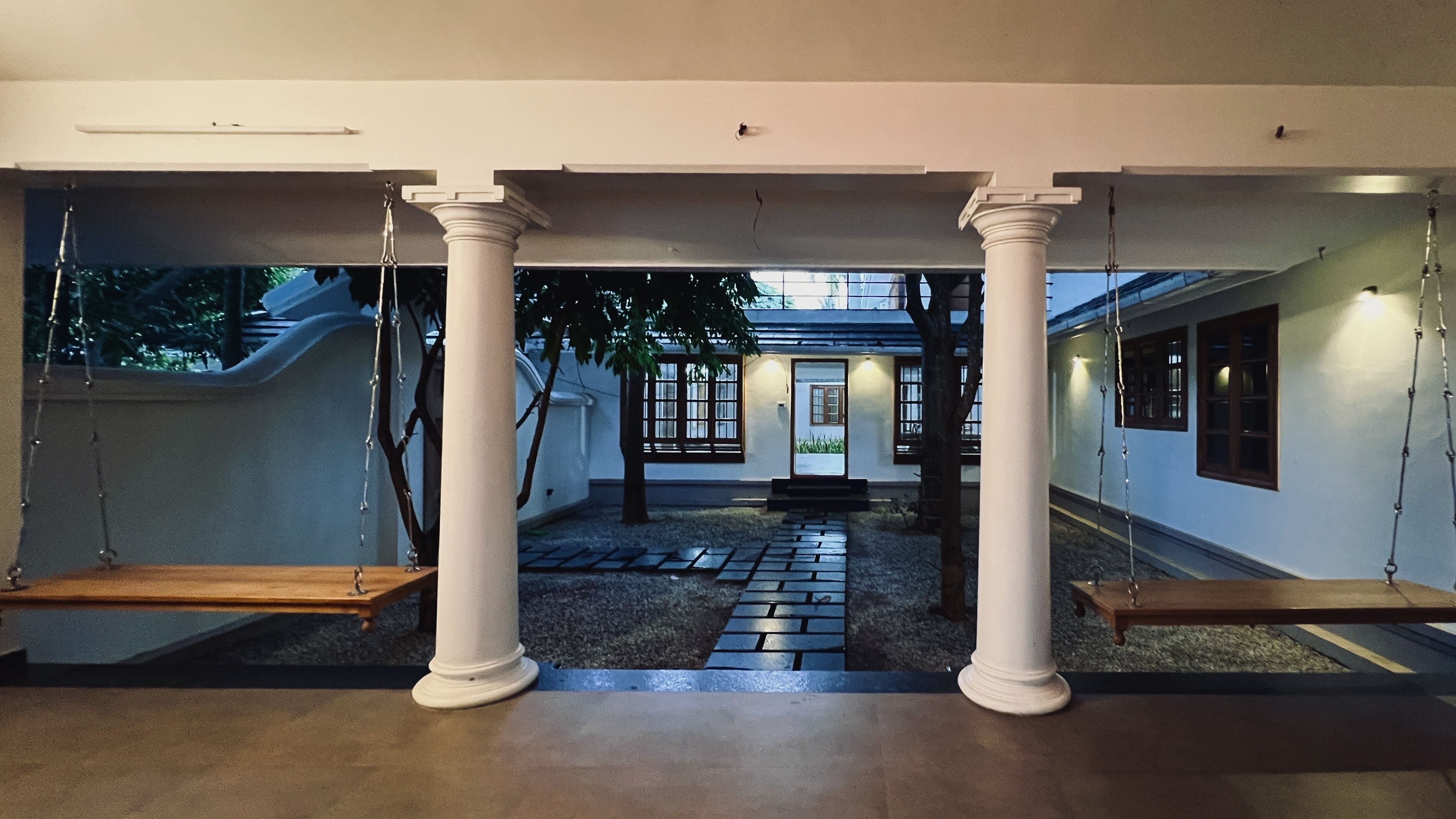 A hallway with white columns, a swing area, and a view of a building with a door and windows.