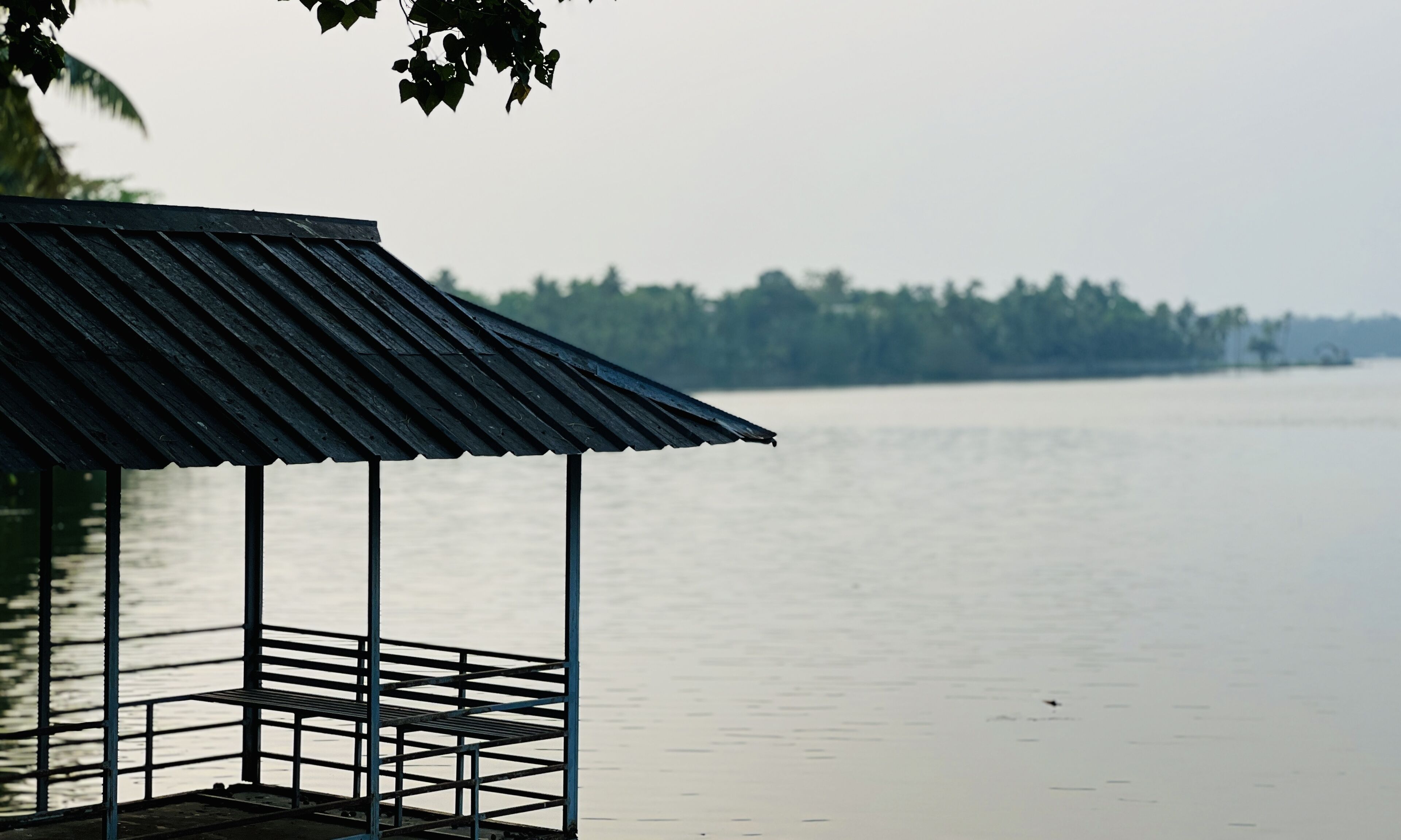 A wooden dock with a metal roof overlooking a calm body of water.
