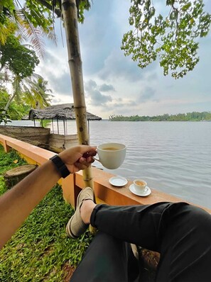 A person sitting by a lakeside with a cup of coffee, overlooking a calm body of water and a distant island.