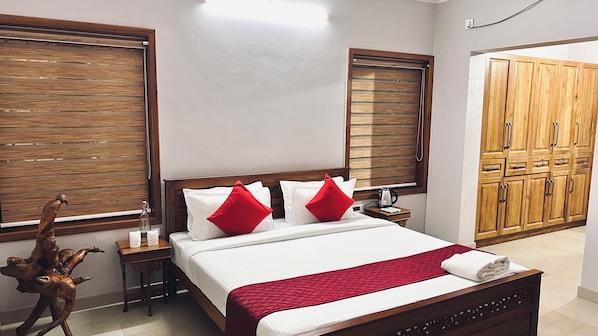 A hotel room with a wooden bed, white bedding, red pillows, a wooden nightstand, a decorative wooden sculpture, and a wardrobe.