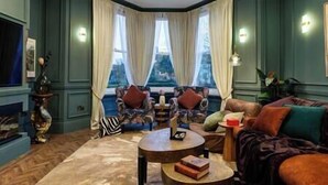 A room with a large window, a sofa, a coffee table, and a decorative vase. - Hob Hurst - Spacious 4 Bed Apt Hot Tub & Parking (Buxton)