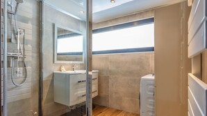 Moderni kylpyhuone, jossa on lasinen suihkuseinä, peilillä varustettu allaskaappi ja seinään upotettu wc-istuin.