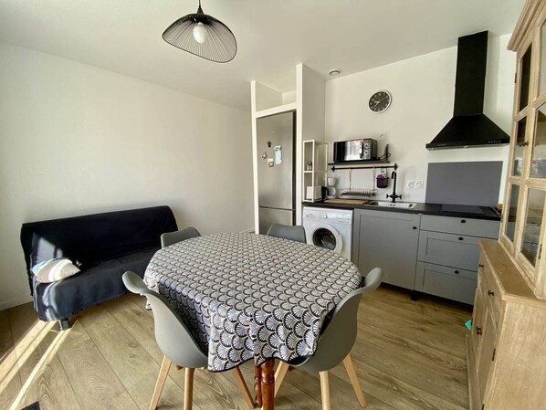 A compact living space with a dining table, chairs, a sofa, a washing machine, a microwave, and a sink. - Comfortable T1 Bis in Itxassou with Garden, Pets Allowed (Itxassou)