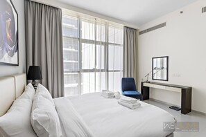A modern hotel room with a large bed, a desk with a chair, and a large window with curtains.