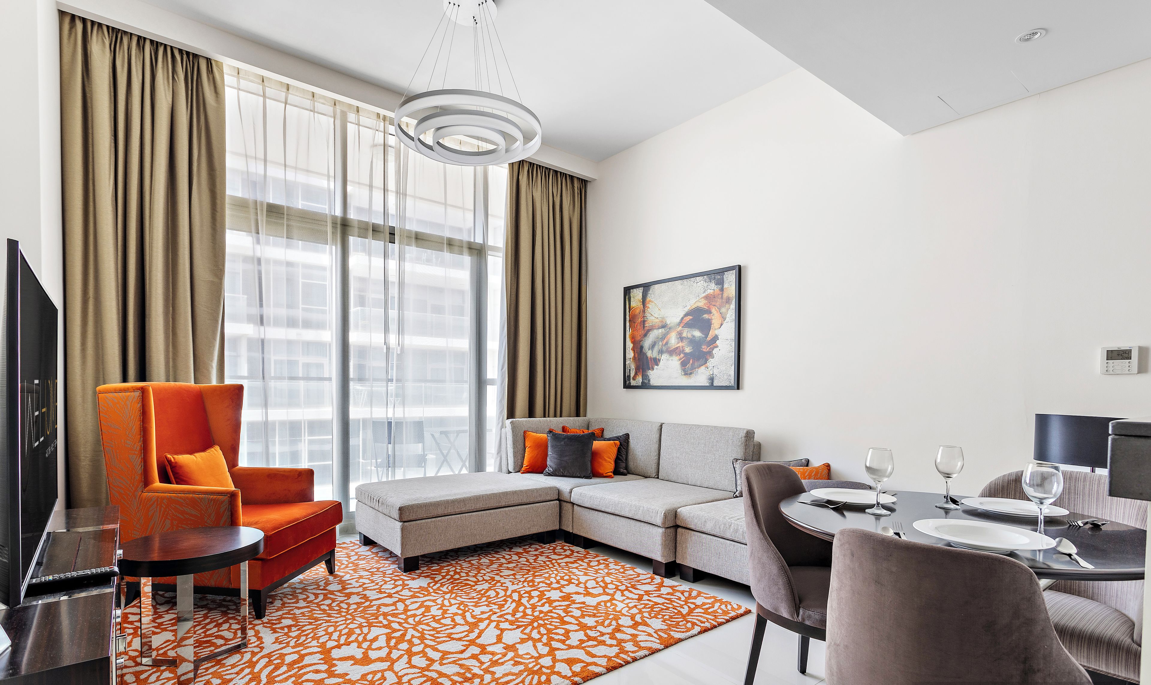 Un salon moderne avec un canapé d’angle, une table à manger avec des chaises et une grande fenêtre agrémentée de rideaux.