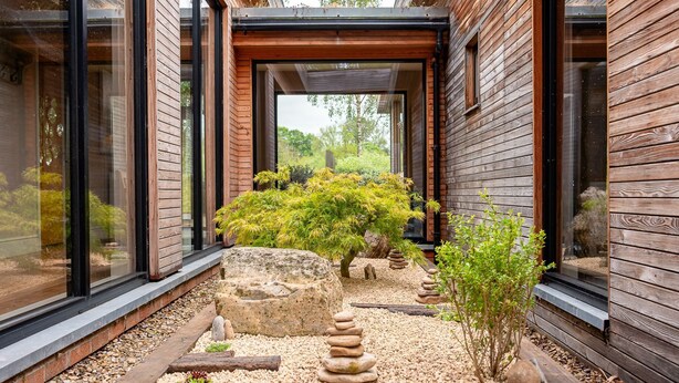 A modern building with wooden exterior walls, a glass entrance, and a landscaped garden with rocks and small trees. - Twenty One -  a lodge that sleeps 12 guests  in 6 bedrooms (Richmond)