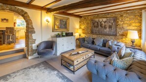 A cozy living room with a stone wall, a wooden ceiling, a grey sofa, a blue armchair, and a wooden coffee table. - Sun Hill Cottage -  a cottage that sleeps 6 guests  in 3 bedrooms (Leyburn)