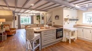 A spacious kitchen with wooden beams, a dining area with wicker chairs, and a view of greenery outside. - Sun Hill Cottage -  a cottage that sleeps 6 guests  in 3 bedrooms (Leyburn)