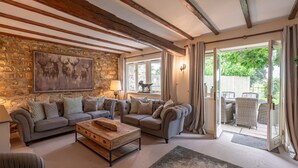 A cozy living room with stone walls, a fireplace, and a large window overlooking a garden. - Sun Hill Cottage -  a cottage that sleeps 6 guests  in 3 bedrooms (Leyburn)