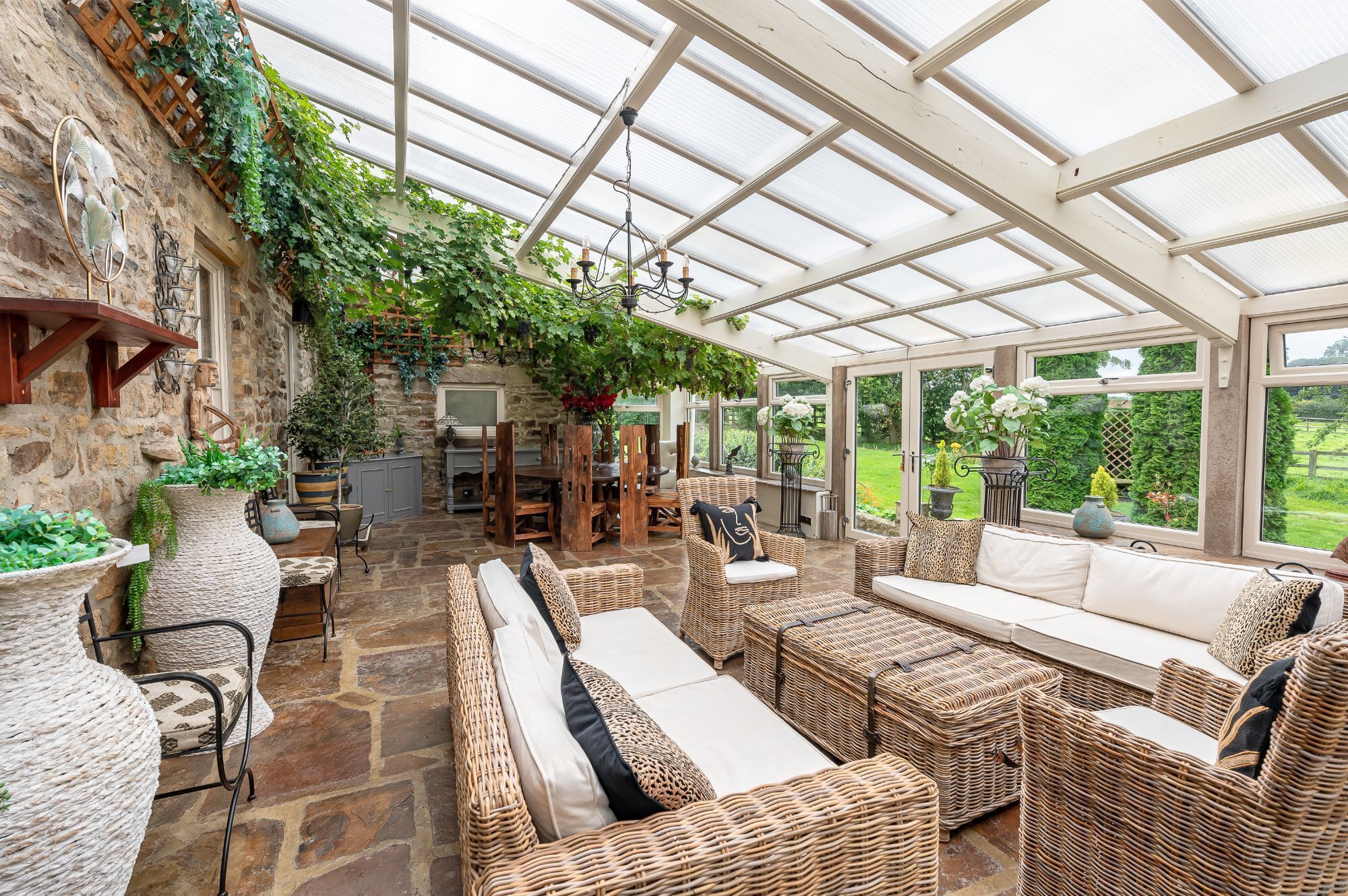 A conservatory with wicker furniture, stone walls, and a view of the garden.