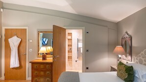 A hotel room with a bed, a dresser, a robe hanging on the door, a mirror, and a bathroom visible through an open door.