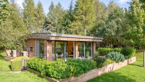 A modern, single-story house with a glass-enclosed patio, surrounded by lush greenery and trees.