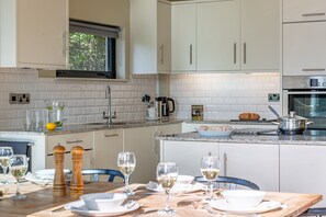 A modern kitchen with white cabinetry, a built-in oven, and a dining area set for a meal.