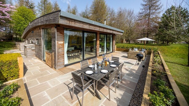 A modern house with a patio area featuring a dining table and chairs, surrounded by a garden.