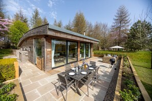 A modern house with a patio area featuring a dining table and chairs, surrounded by a garden.