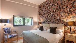 Een slaapkamer met een groot bed, twee nachtkastjes, een stoel en een raam met uitzicht op bomen.