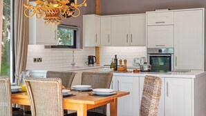 Een moderne keuken met witte kastjes, een houten eettafel, rieten stoelen en een kroonluchter.